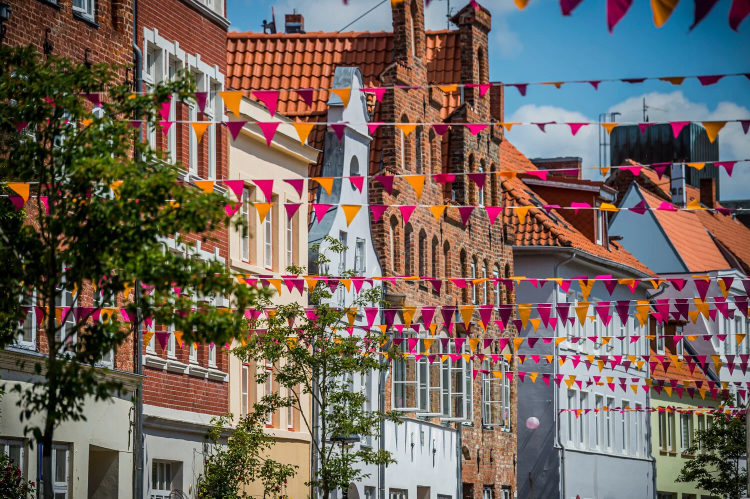 In der Altstadt sind zwischen den Gebäuden mehrere Wimpelketten mit orangenen und pinken Flaggen gespannt